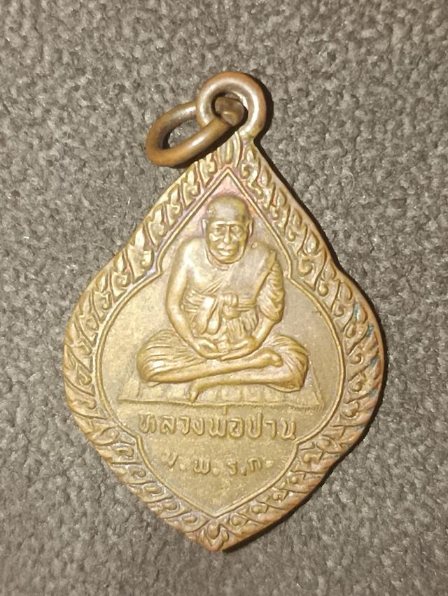 หลวงพ่อปาน วัดมงคลโคธาวาส (วัดบางเหี้ย) จังหวัดสมุทรปราการ รุ่น ม.พ.ร.ก. จัดสร้างขึ้นในปี พ.ศ. 2537ลักษณะเหรียญเป็นทรงพุ่มข้าวบิณฑ์หรือทรงดอกจิก มีหูใ
