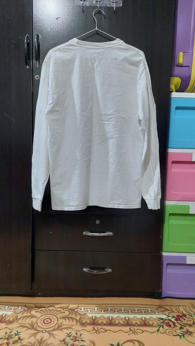เสื้อยืดแขนยาวสีขาว มีสกรีนลายกราฟิกรูปใบพืชขนาดใหญ่ในกรอบสี่เหลี่ยมสีสันแนวไซเคเดลิก (psychedelic) และมีข้อความ "Buzz City GAS" อยู่ด้านล่าง รูปย่อยที่ 2