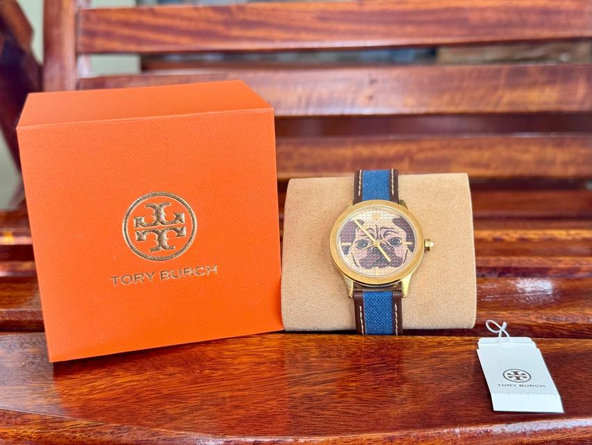 นาฬิกา Tory Burch รุ่น The Gigi Pug ที่มีหน้าปัดลายสุนัขพันธุ์ปั๊กและสายผ้าสีน้ำเงินขอบหนัง